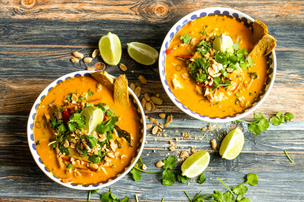 Vegan Tom Yum Soup . A photo showing two portions of the Vegan Tom Yum Soup decorated with lime, peanuts and corriander on a wooden background.